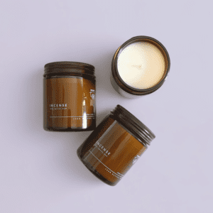 Three brown glass jars containing soy wax candles, two of them lying down with their lids on, the third open and seen from above.
